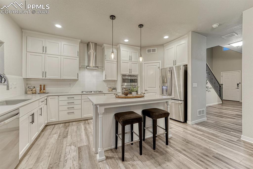 Kitchen featuring a kitchen bar, stainless steel appliances, white cabinetry, and pendant lighting