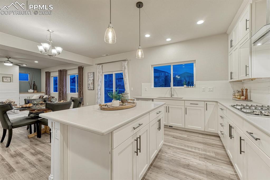 Kitchen featuring open floor plan, white cabinetry, a chandelier, a center island, and decorative backsplash