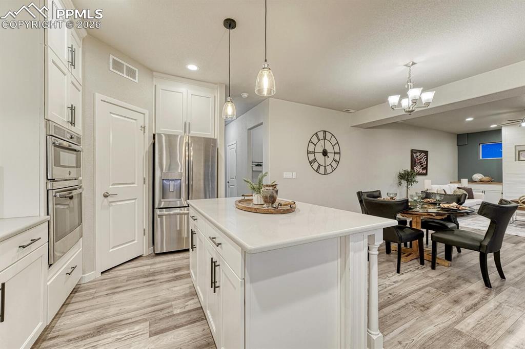 Kitchen with white cabinetry, stainless steel appliances, a center island, hanging lights, and light wood-type flooring