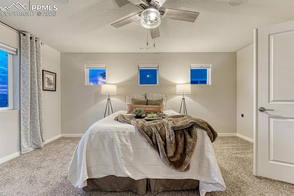 Enter the primary bedroom through stylish French doors with a barn door design, ensuite bathroom, plush carpet flooring, and a ceiling fan.