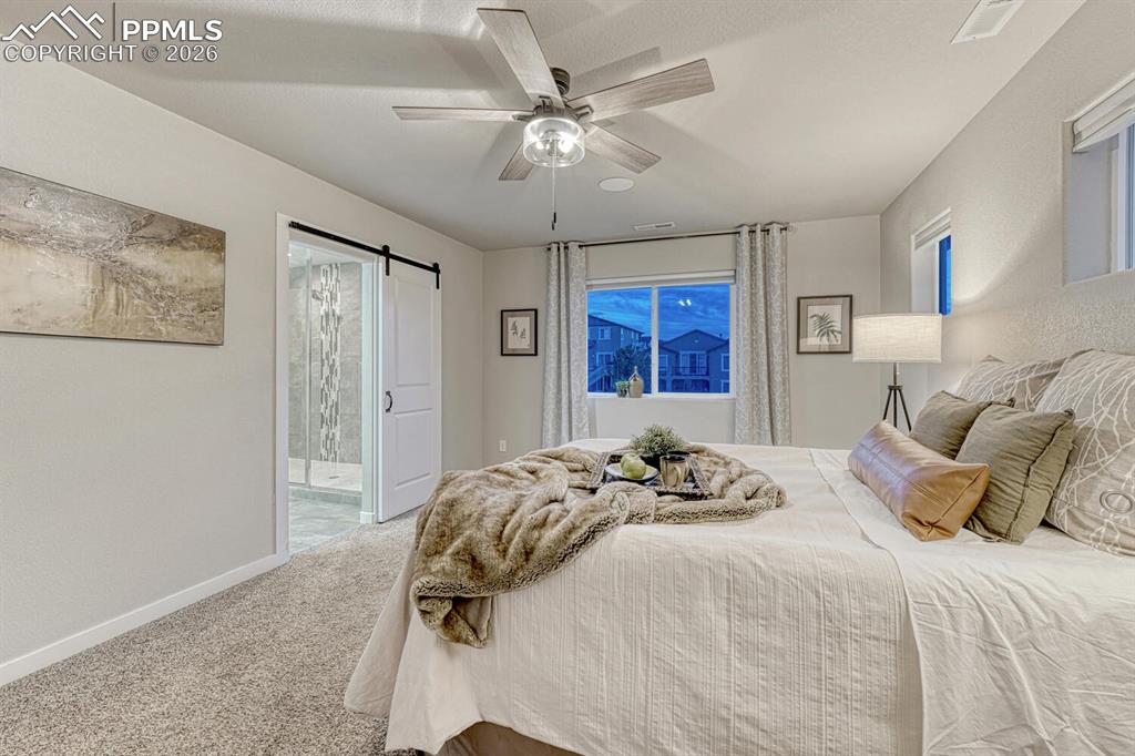 Bedroom with a barn door, carpet flooring, ensuite bathroom, and ceiling fan