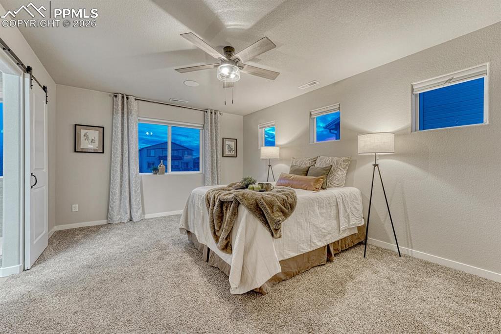 Bedroom featuring a ceiling fan, light colored carpet, a textured wall, a textured ceiling, and a barn door