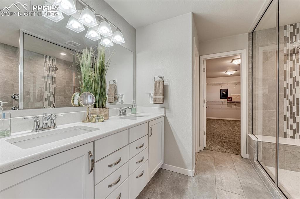 The primary bathroom includes a walk-in shower, double vanity, a large walk-in closet, and elegant light-colored tile floors.