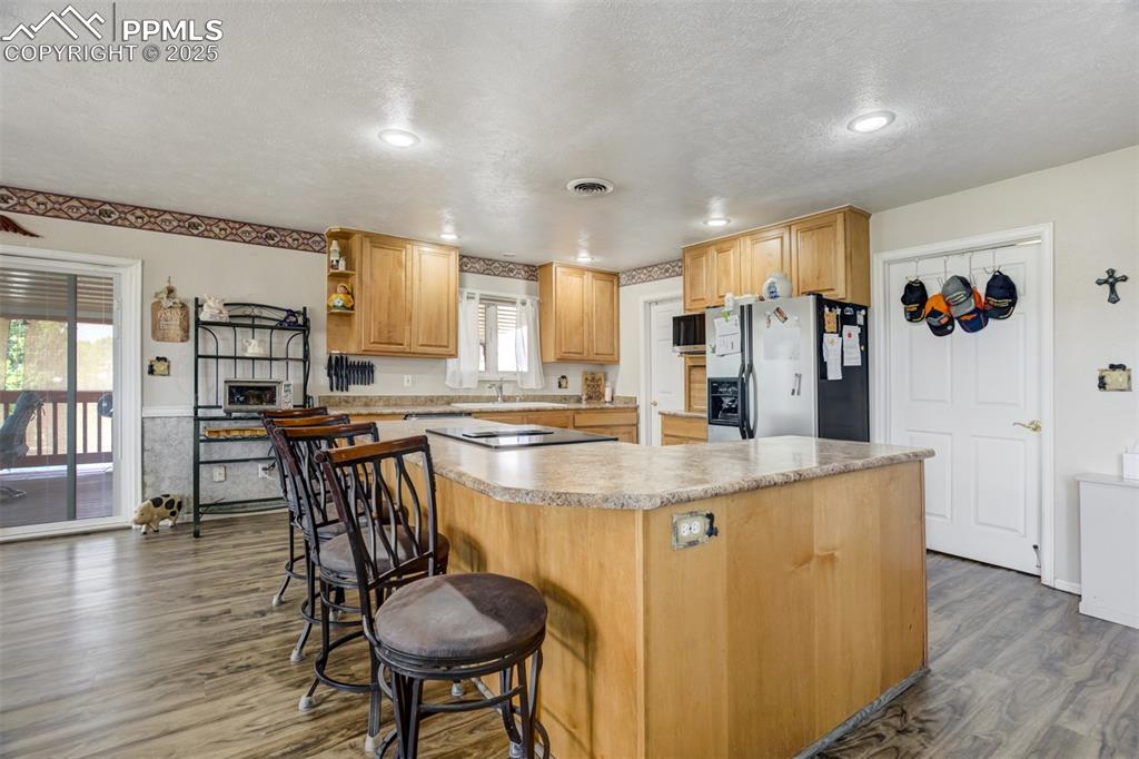 Kitchen with light countertops, open shelves, stainless steel fridge with ice dispenser, dark wood-style floors, and a textured ceiling