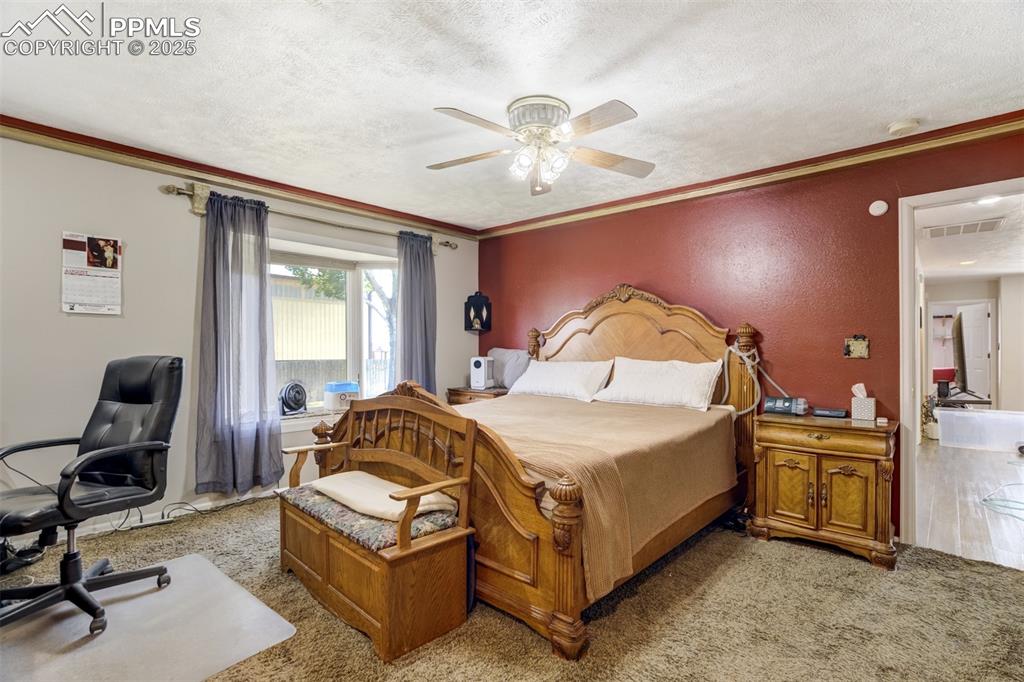 Bedroom with a textured ceiling, ornamental molding, ceiling fan, light colored carpet, and a desk