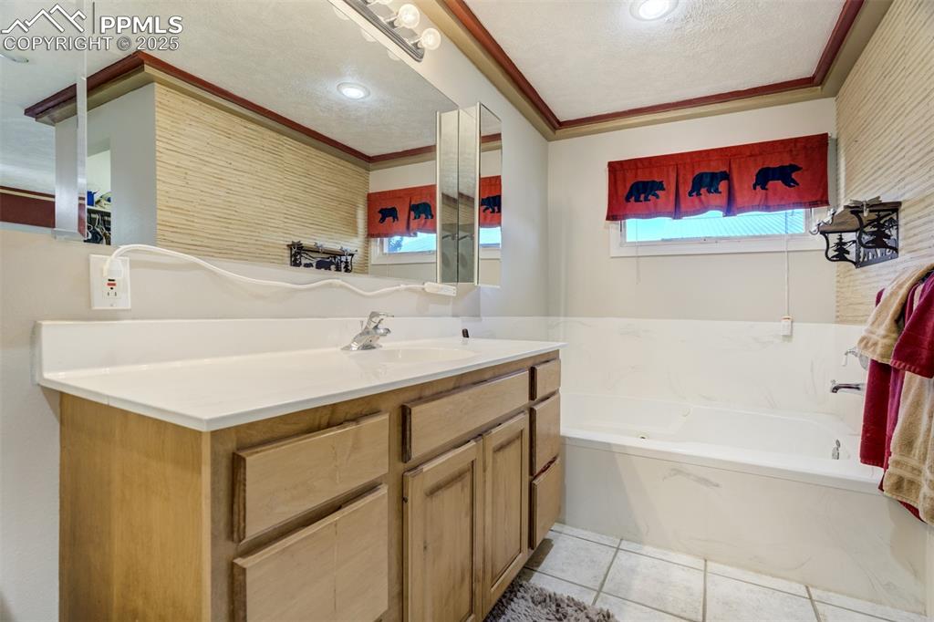 Bathroom with healthy amount of natural light, vanity, a textured ceiling, a garden tub, and crown molding