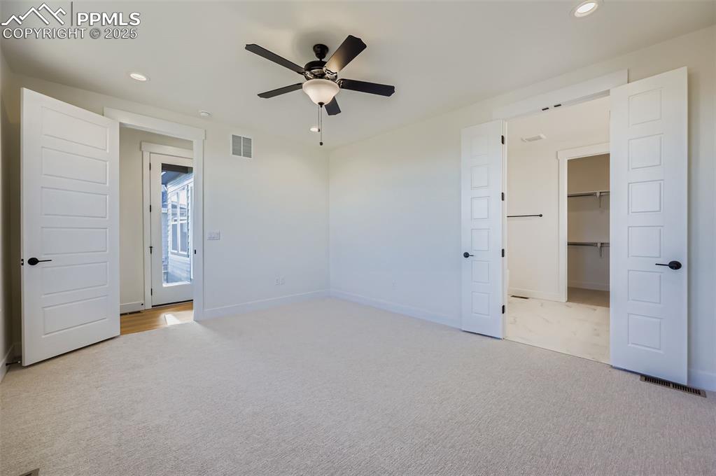 Unfurnished bedroom featuring recessed lighting, a walk in closet, a ceiling fan, and light carpet