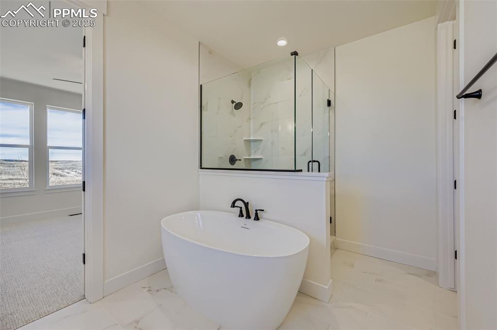 Bathroom featuring a marble finish shower, a freestanding bath, light marble finish flooring, and recessed lighting