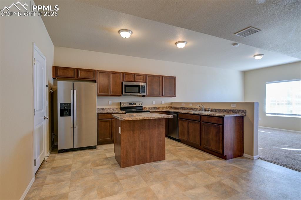 Kitchen with stainless steel appliances, a kitchen island, dark stone counters, and a textured ceiling