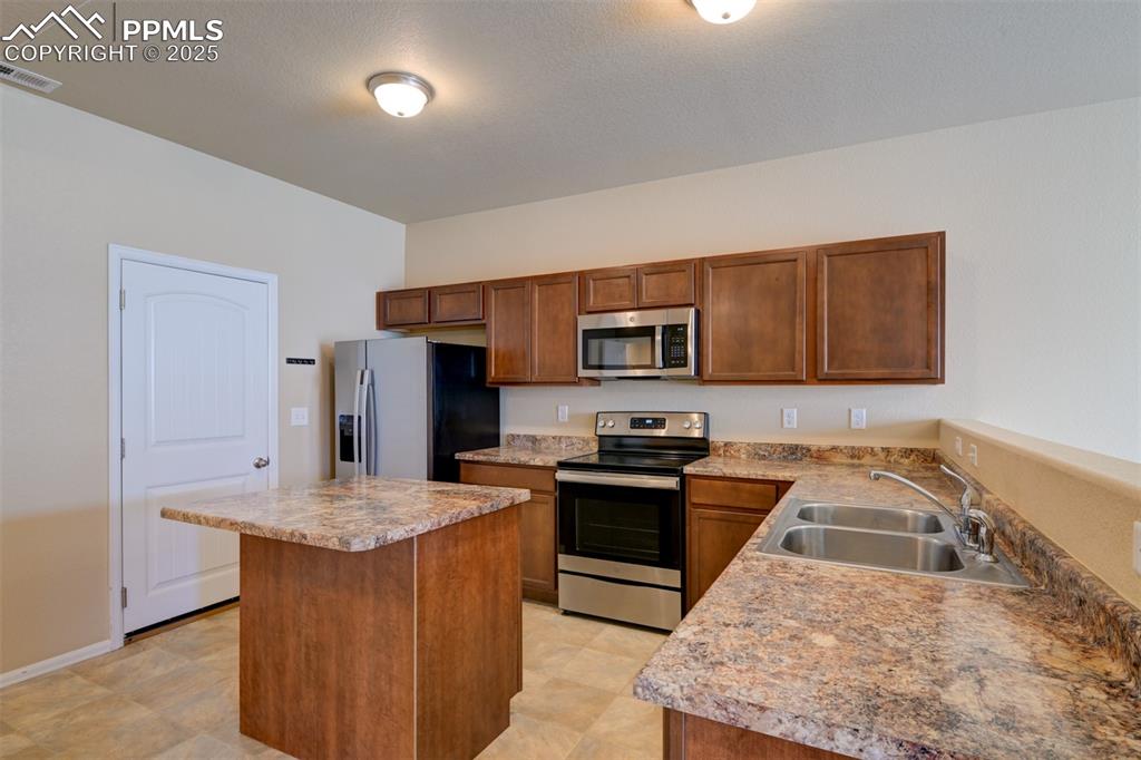 Kitchen with stainless steel appliances, a center island, and brown cabinetry