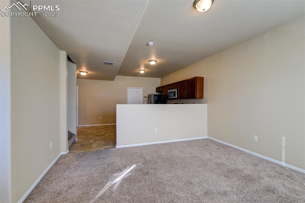 Kitchen with light carpet, open floor plan, dark brown cabinetry, appliances with stainless steel finishes, and light countertops