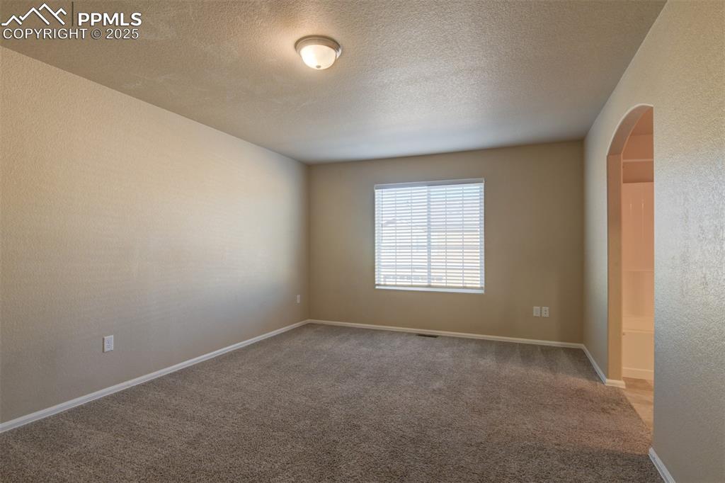 Carpeted empty room with arched walkways, a textured wall, and a textured ceiling