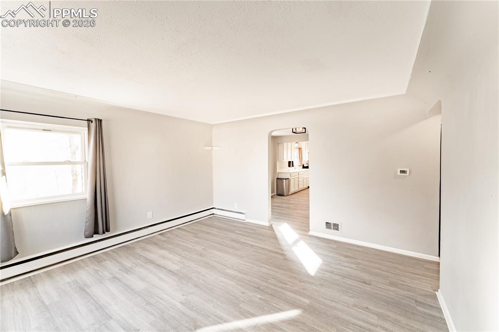 Empty room featuring arched walkways, light wood-style flooring, a baseboard radiator, and a textured ceiling
