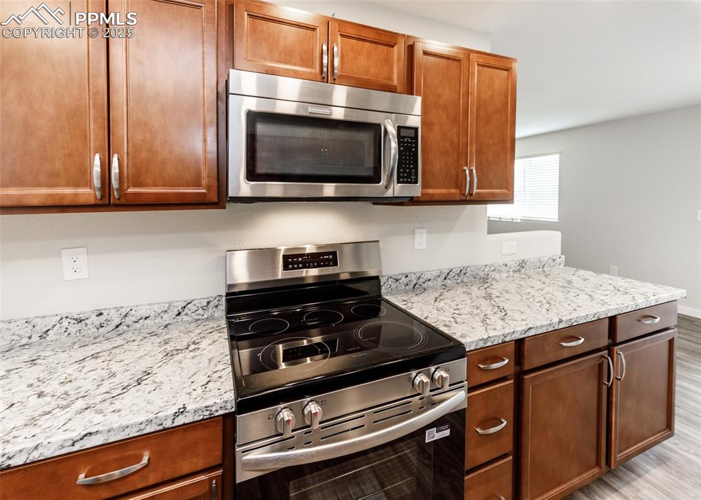 Kitchen featuring appliances with stainless steel finishes, brown cabinetry, light stone counters, and light wood finished floors