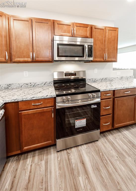 Kitchen featuring stainless steel appliances, brown cabinetry, and light wood finished floors