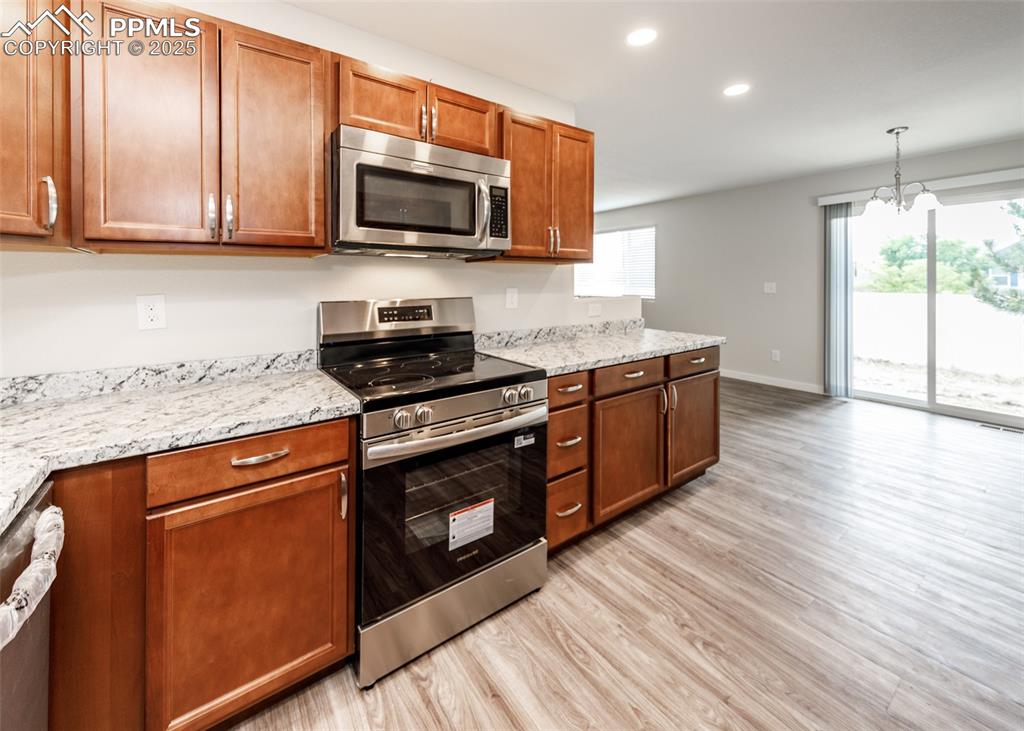 Kitchen featuring stainless steel appliances, brown cabinets, light wood finished floors, recessed lighting, and light stone counters