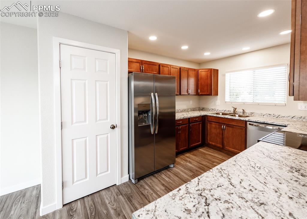 Kitchen with appliances with stainless steel finishes, light stone countertops, light wood-style flooring, recessed lighting, and brown cabinetry