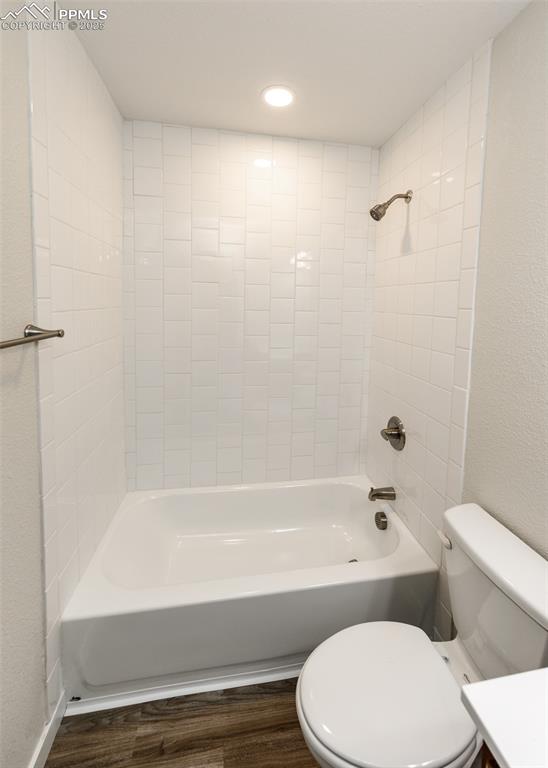 Full bathroom with  shower combination, a textured wall, dark wood finished floors, vanity, and recessed lighting