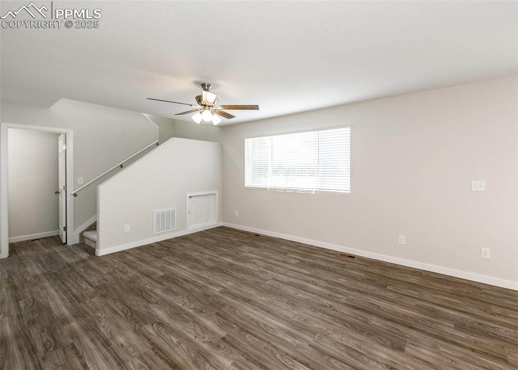 Unfurnished living room featuring dark wood-type flooring, stairway, and a ceiling fan