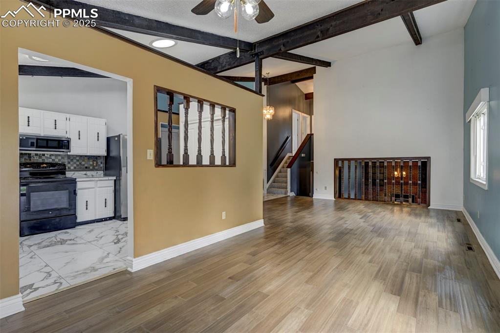 Unfurnished living room with a ceiling fan, beamed ceiling, stairs, and light wood-type flooring
