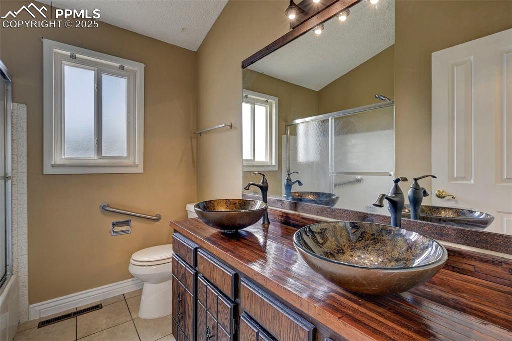 Full bathroom with tile patterned floors, a textured ceiling, vaulted ceiling, and double vanity