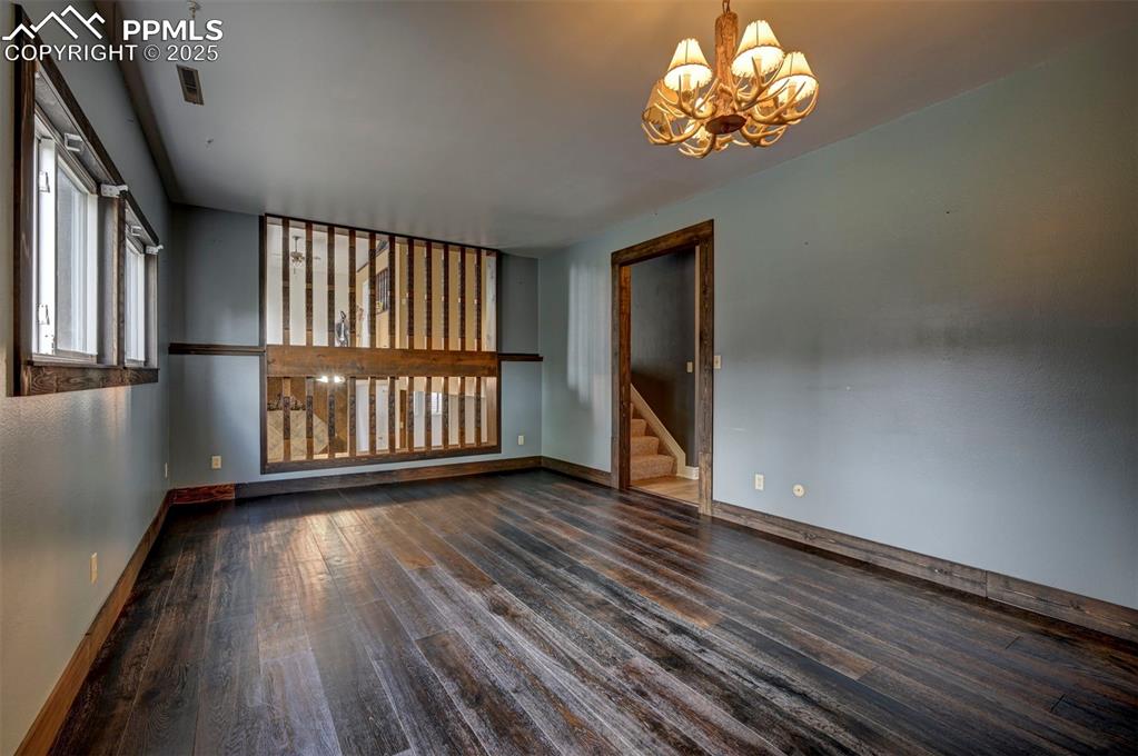 Empty room featuring a chandelier, wood finished floors, and stairs