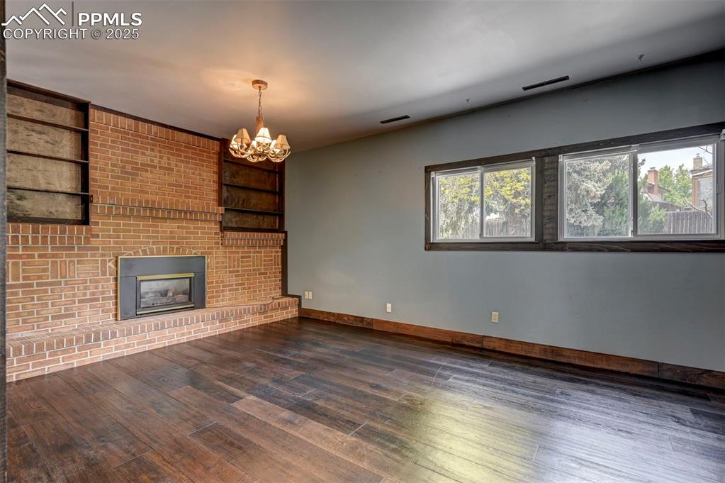 Unfurnished living room with wood finished floors, a chandelier, a fireplace, and built in features