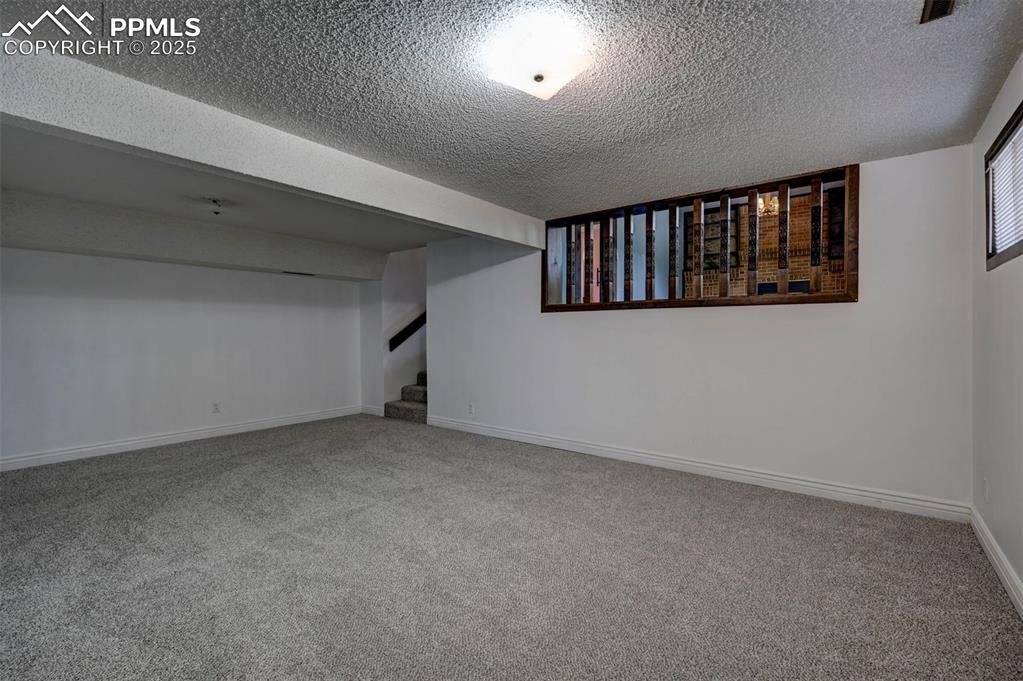 Finished basement with a textured ceiling, carpet floors, and stairway