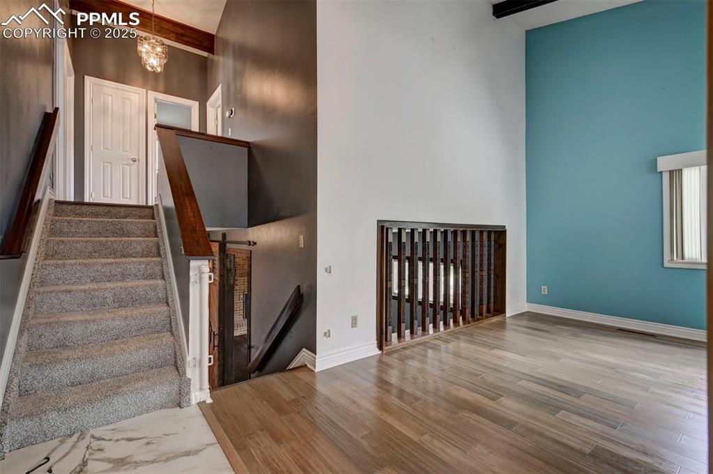 Staircase with a high ceiling, wood finished floors, a chandelier, and beam ceiling