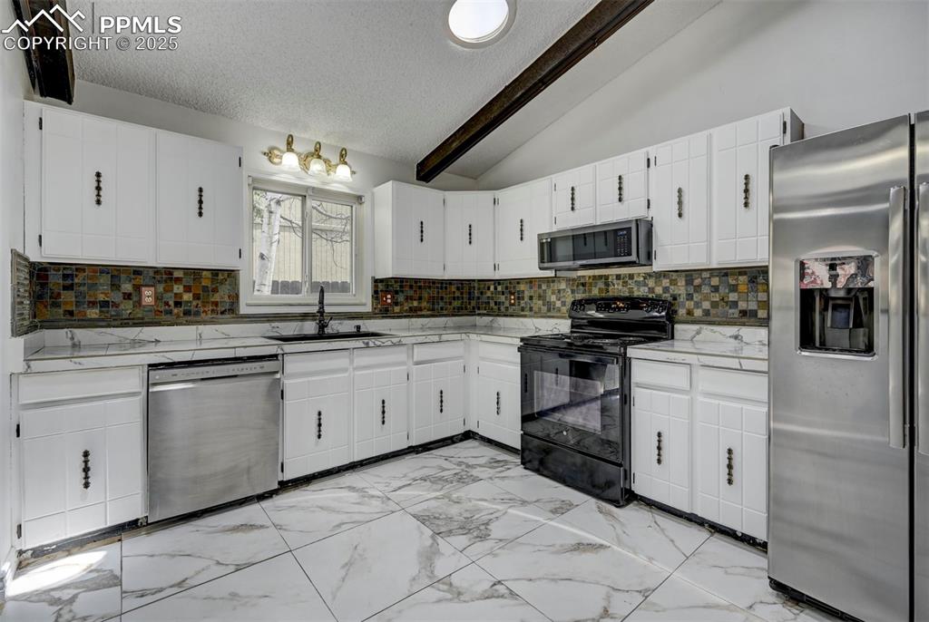 Kitchen featuring stainless steel appliances, a textured ceiling, decorative backsplash, white cabinetry, and light marble finish flooring