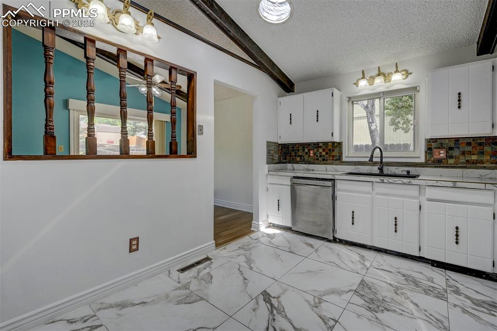 Kitchen with stainless steel dishwasher, backsplash, lofted ceiling, white cabinetry, and a textured ceiling