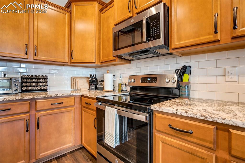 Kitchen with stainless steel appliances, light stone countertops, wood finish cabinetry, and tasteful backsplash.