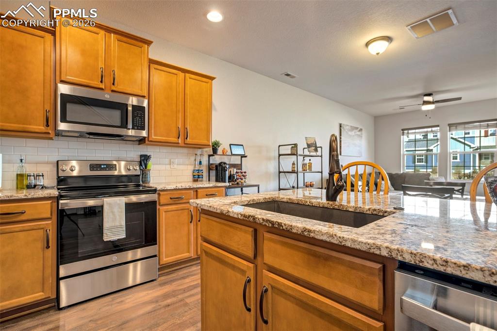 Kitchen featuring stainless steel appliances, light stone countertops, wood finish cabinets.