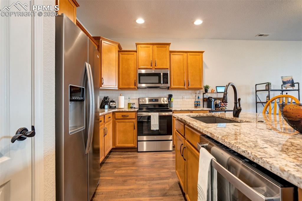 Kitchen area featuring stainless steel appliances, wood finish cabinetry, light stone counters, and recessed lighting