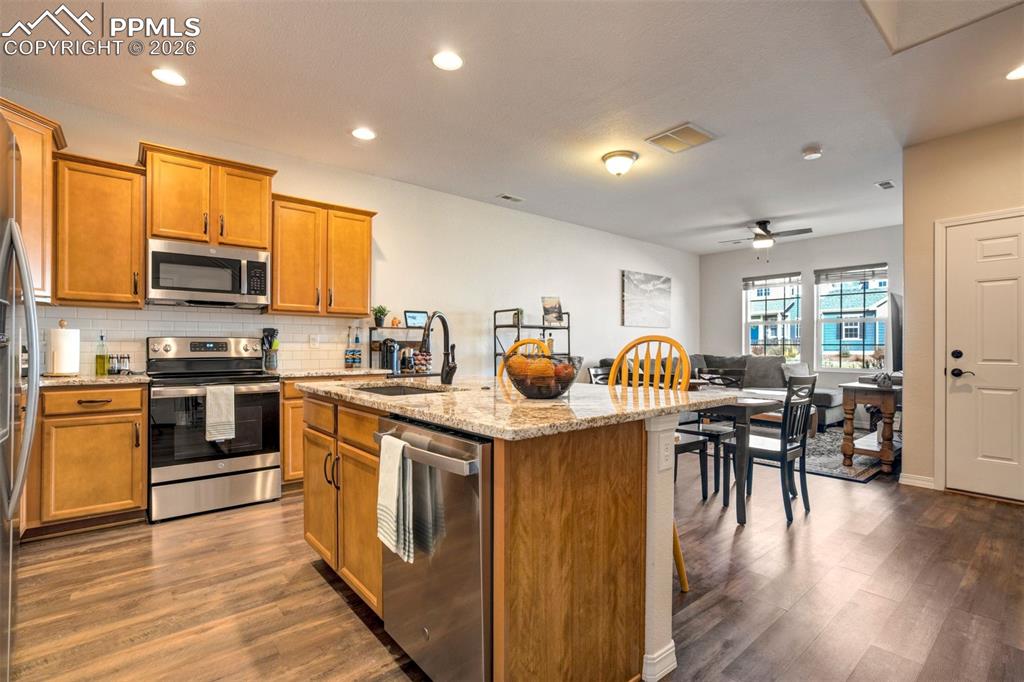 Kitchen with stainless steel appliances, light stone countertops, kitchen island with sink, and recessed lighting.  Front door on the right of the photo. 