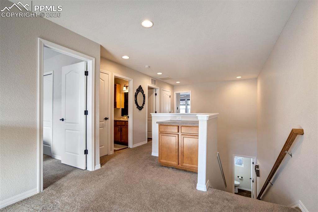 Hallway with an upstairs landing, recessed lighting, and light carpet