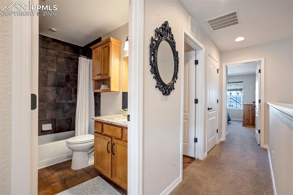 Hallway bathroom showing the bath/shower and sink with stone countertop.  Tile flooring. 