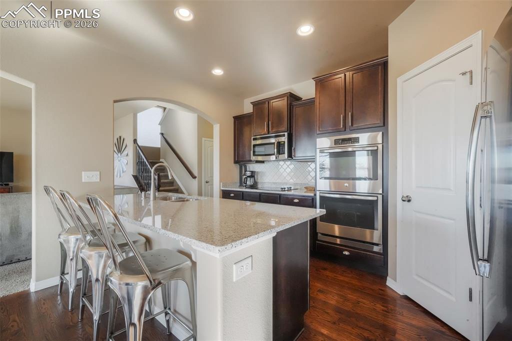 Kitchen with stainless steel appliances, granite counters, double wall ovens, cooktop, bar seating and dining area