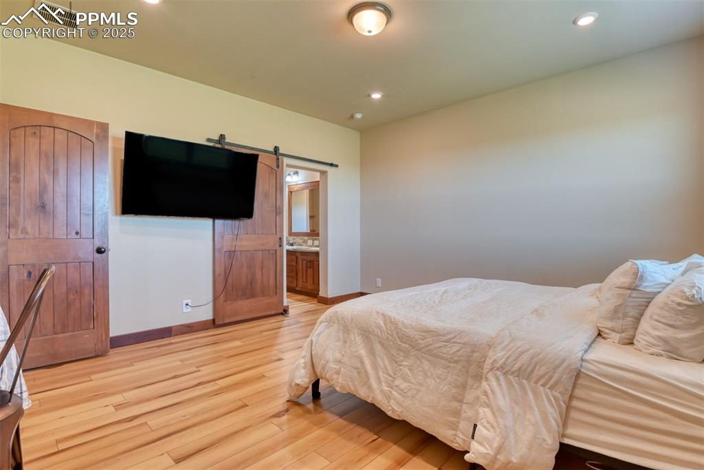 Bedroom with LVT wood style floors, a barn door, recessed lighting, and ensuite bath