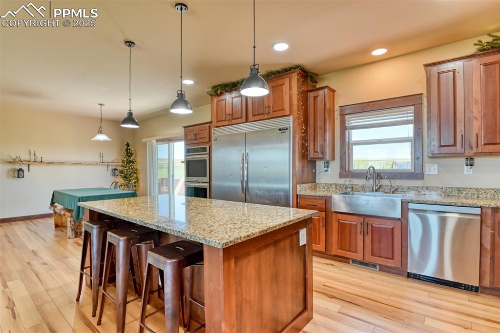 Kitchen featuring stainless steel appliances, brown cabinets, light stone counters, a kitchen island, and healthy amount of natural light