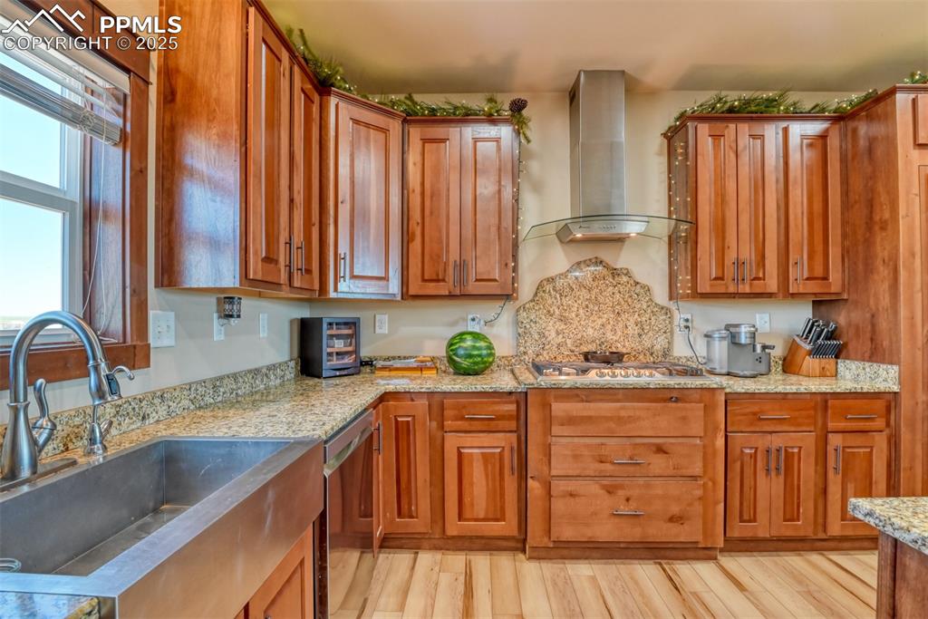 Kitchen with wall chimney range hood, appliances with stainless steel finishes, light wood-type flooring, and brown cabinetry