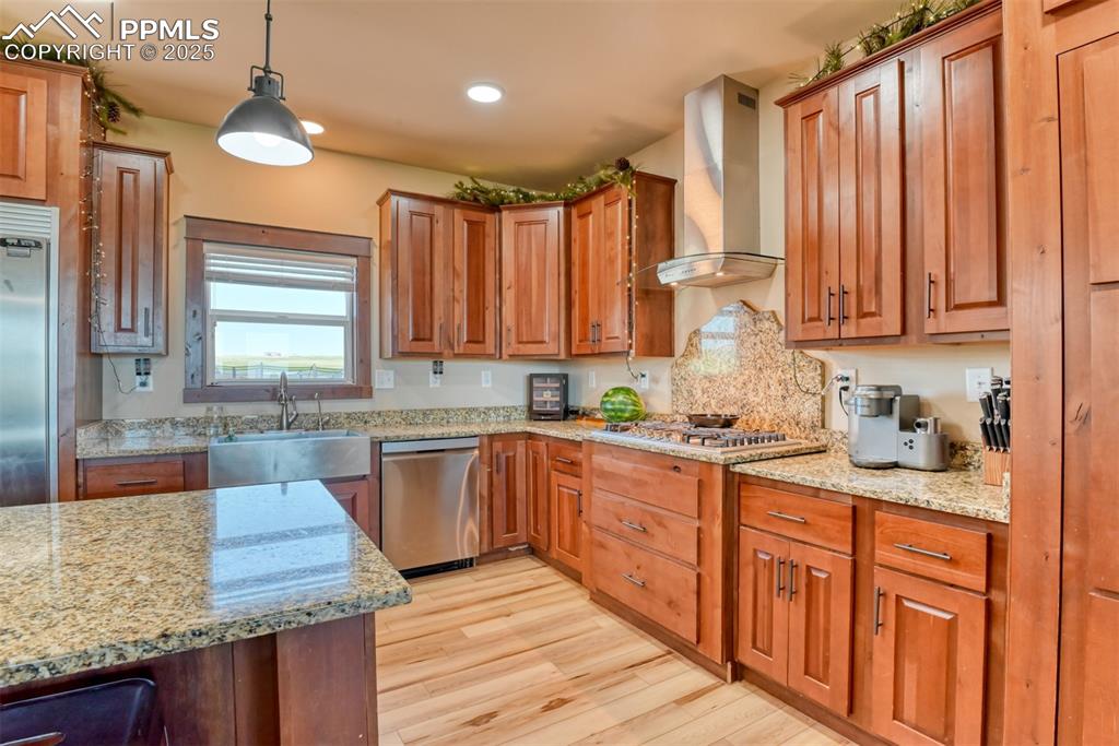 Kitchen with wall chimney range hood, light wood-style flooring, appliances with stainless steel finishes, light stone countertops, and recessed lighting