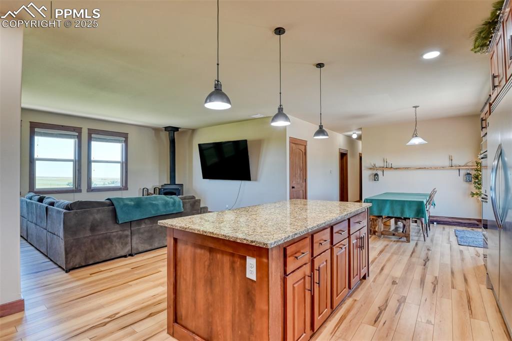 Kitchen with a wood stove, light wood-style floors, light stone counters, a kitchen island, and recessed lighting