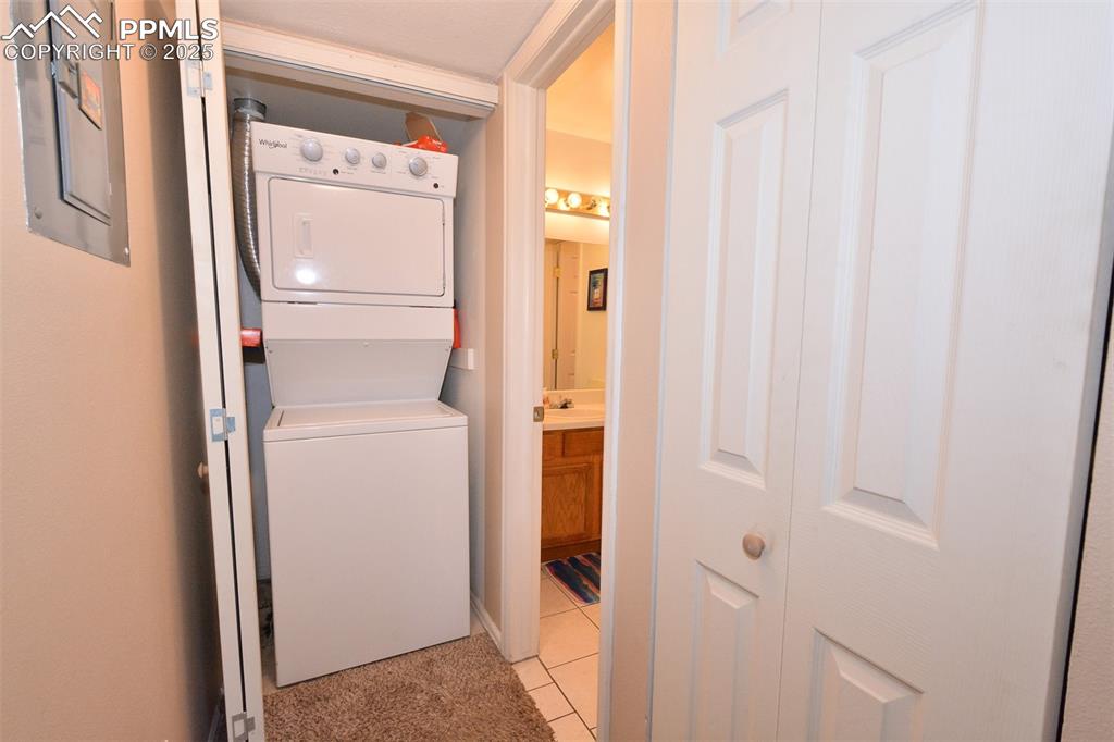 Clothes washing area featuring light tile patterned floors, stacked washer and dryer, laundry area, and electric panel