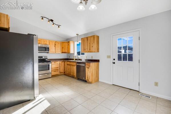 Kitchen with stainless steel appliances, hanging light fixtures, dark countertops, vaulted ceiling, and light tile patterned flooring