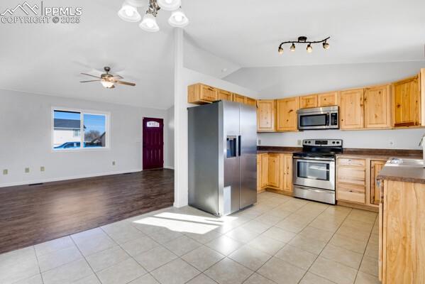 Kitchen with light tile patterned floors, stainless steel appliances, dark countertops, lofted ceiling, and light brown cabinetry