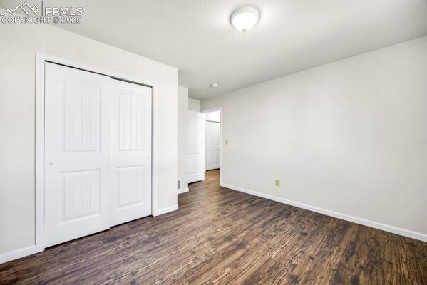 Unfurnished bedroom featuring a closet and dark wood-style flooring