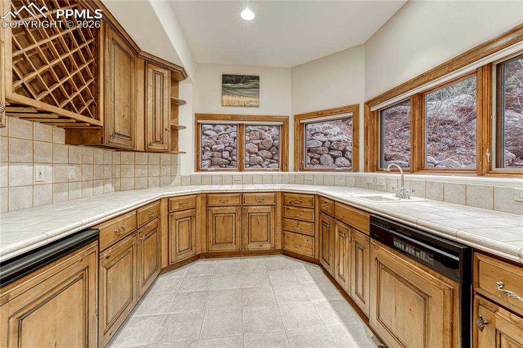 An expansive lower level wet bar with natural light, generous storage, a dishwasher, and a beverage refrigerator.