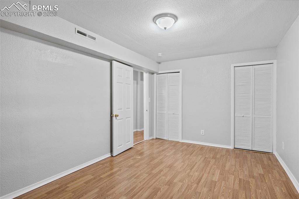 Bedroom with two closets, light wood-style floors, and a textured ceiling