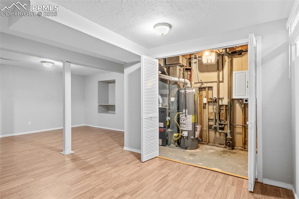 Finished basement featuring a textured ceiling, water heater, light wood finished floors, and heating unit